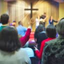 Christian congregation worshipping together with a cross emitting light rays in the background