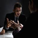 Man talking to a handcuffed person within a dimly lit room