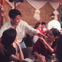 A young man patting his friends on their shoulders as a greeting upon encountering them at a restaurant.