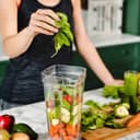 A girl making green detox cocktail of fresh vegetables and fruits.