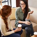 Two women engaged in conversation over coffee, while sitting in a coffee shop.