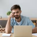 Tired young man looking at his laptop, seemingly exhausted and unmotivated.
