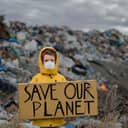 A child with a face mask holding a Save our planet board at a landfill