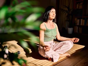 A woman practicing meditation in her room during a sunny day