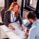 two business professionals, a man and a woman, sitting at an office table, finalizing and signing a contract