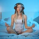 Woman meditating in her bed while wearing headphones
