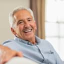 Portrait of happy senior man smiling at home. Old man relaxing on sofa and looking at camera. Portrait of elderly man enjoying retirement