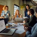 A business meeting of young, diverse colleagues, seated around a big table within an office environment.