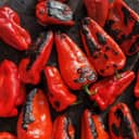 Close-up of red peppers roasting on a wood-burning stove, showing their charred surface.