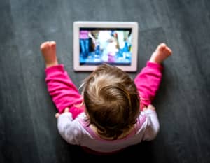 A little bored girl watching a cartoon on a tablet in a living room