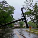 Broken utility pole hanging above a road after storm