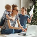 An exhausted young mom trying to focus on her laptop and paperwork on the couch with her small children.