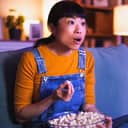 Asian woman at home late at night, eating popcorn and watching TV with a surprised face expression