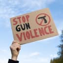 woman holding a sign with a "Stop Gun Violence" slogan and an image of a black pistol with a strike-through at the protest