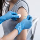 Close-up of a patient's arm while a doctor or nurse is injecting a vaccine using a syringe.