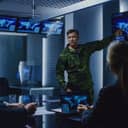 A high-ranking military officer delivers a briefing to a group of government agents and politicians.