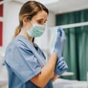 A female nurse wearing a facemask adjusting her sanitary gloves