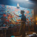A skilled female artist paints an abstract oil piece with sweeping brush strokes on a big canvas in her studio.
