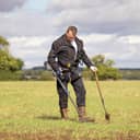 Treasure hunter sweeping a field with a metal detector in search of buried artifacts or valuables.