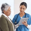 Close-up of a healthcare professional showing the test results to an elderly woman using a tablet.