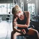 Woman in gym painfully holding her arm with a dumbbell resting on her leg