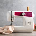 Close-up of a white sewing machine set up with beige fabric and various crafting tools on a wooden table.