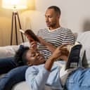 young couple, positioned comfortably on a couch in their living room, reading books