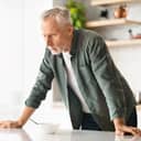 upset senior man leaning on a kitchen table with a white bowl in front of him, looking away deep in thought