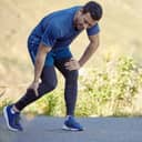 Young man experiencing a sharp calf pain or cramp while running along a mountain trail in nature.