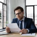 A worried businessman at his desk, reading a letter with troubling news or other negative correspondence.