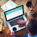 A closeup view of a man sending a job application on his laptop while holding a cup of coffee in his other hand