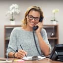 a smiling woman talking on the phone and taking notes at her office desk