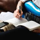 young man holding guitar and writing a song in his notebook