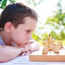 Small boy looking closely at chess pieces on table outdoors
