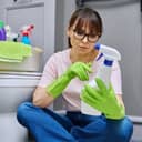 woman examining the label of a spray cleaner, reading instructions while seated on a bathroom floor