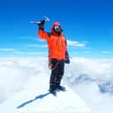 A mountaineer standing at the top of a mountain holding his icepick triumphantly above his head