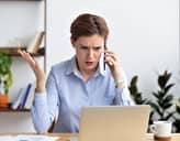 A female visibly irritated talking on the phone and looking at a laptop