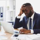 stressed young male entrepreneur because of poor time management skills, sitting in the office, working on laptop and touching his forehead