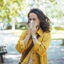young woman blowing her nose in a park, allergies season