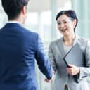 Asian businesswoman smiling and shaking hands with younger businessman in an office corridor