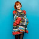 Cheerful young woman in an oversized sweater, standing against a blue background.