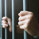 Person clutching the bars of a prison cell