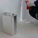 close-up of a gallon of paint thinner beside an old wall, with a painter clearing sticky residue in the corner