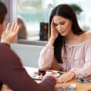 close-up of a young couple arguing at a cafe, woman holding her hand on her forehead