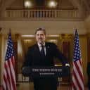 confident politician smiling for cameras at a White House press conference with US flags in the background
