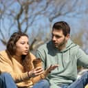 young couple arguing while sitting in the park, woman is holding a paper cup of coffee