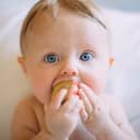Baby with blue eyes trying to stuff a toy brick into their mouth