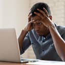 A man looking at a lap top in disbelief holding his head with his hands