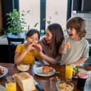 Two kids enjoying croissants for breakfast with their mom in a modern kitchen at home.