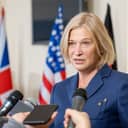 Female politician in elegant suit speaking in microphones at press conference